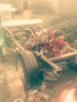1991 Ford Bronco - The chassis and engine of a vehicle are visible in an outdoor setting, possibly a backyard or workshop. The engine appears to be red and is…