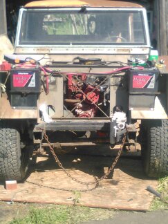 1991 Ford Bronco - The front of a vintage vehicle, possibly a Land Rover Series, is shown with its hood removed, revealing the engine. Two batteries are mount…