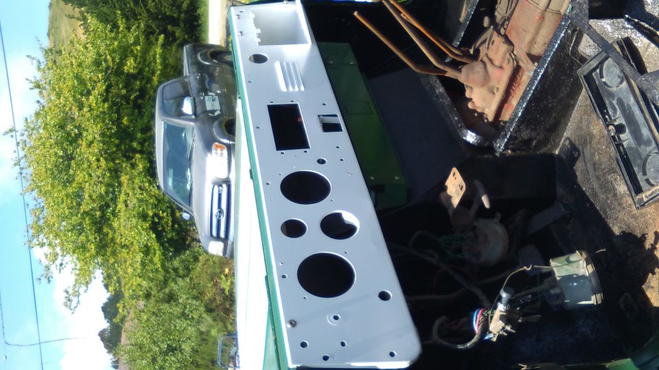 White dashboard panel with circular cutouts in a truck bed, with a gray SUV and trees behind.