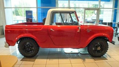 1991 Ford Bronco - A red 1970s International Harvester Scout II pickup truck with a white roof is parked indoors on a tiled floor, likely in a dealership show…