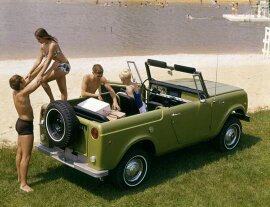 1991 Ford Bronco - A green convertible SUV is parked on a grassy area near a body of water with people in swimsuits around it. The vehicle has a spare tire mo…