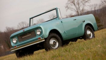1991 Ford Bronco - A light blue convertible SUV is parked on a grassy incline, angled towards the viewer's left. The vehicle features a chrome grille, round h…