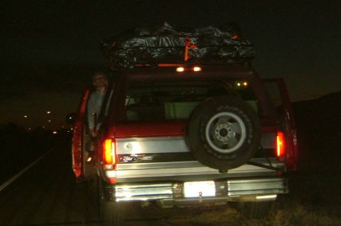 1996 Ford Bronco - A red SUV is parked at night with its rear facing the camera, loaded with luggage on its roof rack.