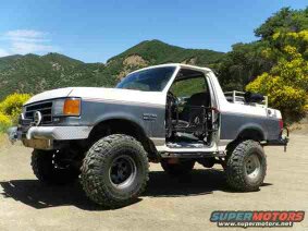 1991 Ford Bronco - A lifted 1991 Ford Bronco with the doors removed sits on a dirt road with a mountainous, tree-covered landscape in the background. The vehi…
