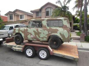 1991 Ford Bronco - A vintage SUV with a camouflage paint scheme is loaded onto a flatbed trailer in a residential driveway. The vehicle appears to be an Inter…