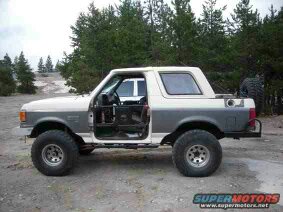 1991 Ford Bronco - A lifted 1991 Ford Bronco with the driver's side door removed sits in a dirt lot with trees in the background. The vehicle has large off-ro…