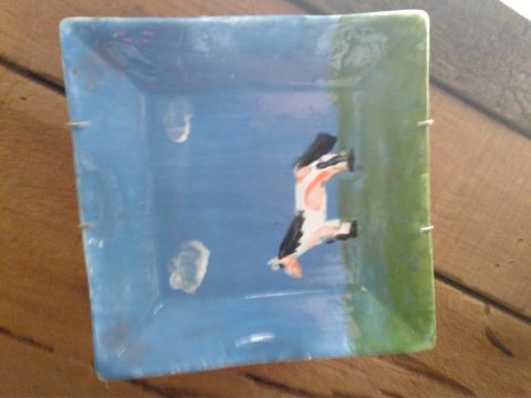 1991 Ford Bronco - A ceramic dish with a painting of a cow on it. The dish is square with blue and green painted sides and has metal fasteners on the edges.