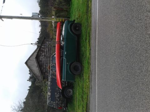 1991 Ford Bronco - A dark green vehicle with a red kayak strapped to its roof is parked next to a road and a wooden building. A camouflage-patterned truck bed…