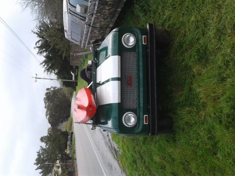 1991 Ford Bronco - A green and white vintage SUV with a red kayak mounted on the rear is parked on the side of a wet road next to a grassy area. A camouflage-…