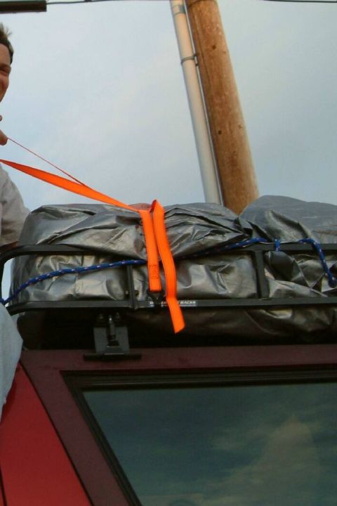 1996 Ford Bronco - A person secures cargo on a roof rack of a red SUV with orange straps.