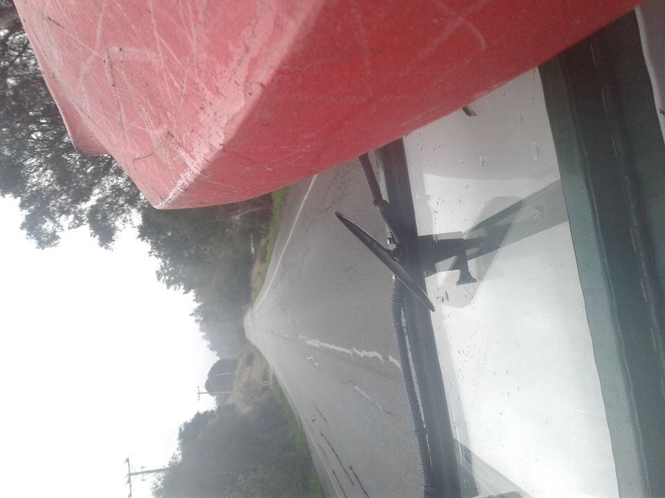 Red kayak on vehicle roof, viewed through windshield on a wet road.
