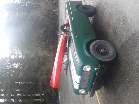 1991 Ford Bronco - A green vintage SUV with a red kayak strapped to its roof is parked on a wet asphalt surface next to trees.