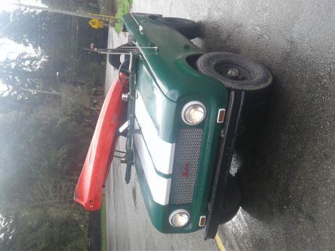 1991 Ford Bronco - A green vintage SUV is parked on a wet asphalt surface, carrying a red kayak on its roof rack. The vehicle has a white stripe on the hood a…