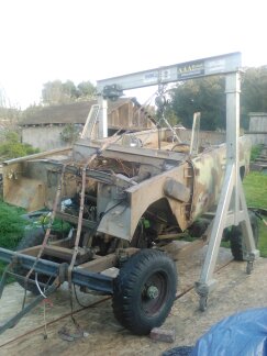 1991 Ford Bronco - A heavily disassembled vehicle, possibly a 1991 Ford Bronco, is suspended by a gantry crane. The body and chassis are exposed, revealing th…