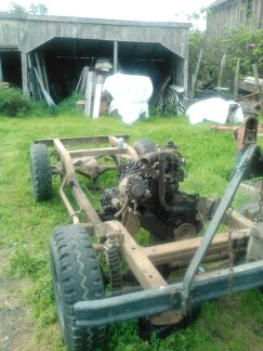 1991 Ford Bronco - The chassis and engine of a vehicle are shown in an outdoor setting. The vehicle appears to be a frame with suspension components, wheels,…
