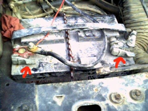 1986 Ford Bronco - Close-up of a car battery's corroded terminals, with red arrows highlighting connection points.