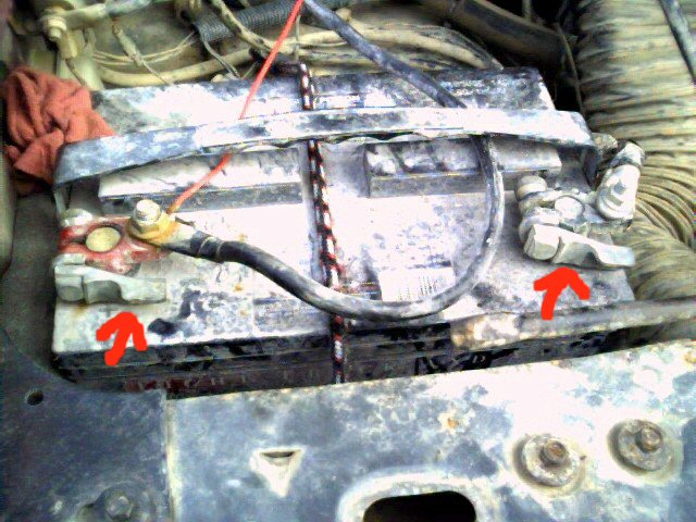 Corroded car battery terminals with red arrows pointing to them