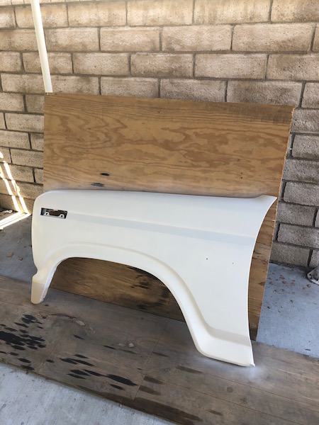 1981 Ford Bronco - A white fiberglass fender flare is leaning against a wooden board, which is propped up against a brick wall. The fender flare appears to be…