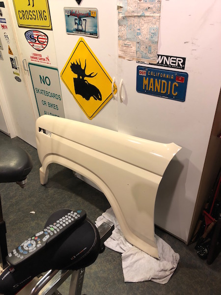 1981 Ford Bronco - A cream-colored vehicle fender is leaning against a wall covered in various signs and a map. A remote control rests on the seat of a statio…
