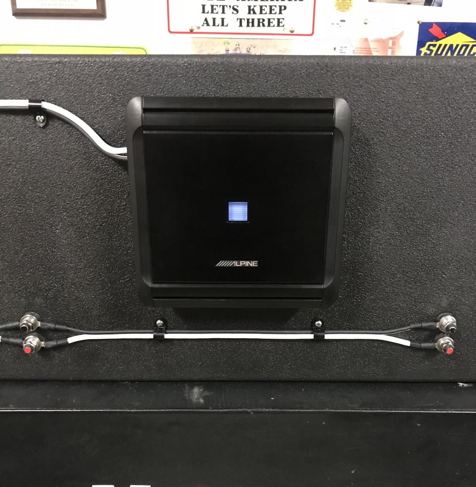 Black Alpine amplifier mounted on a textured surface with wires below.