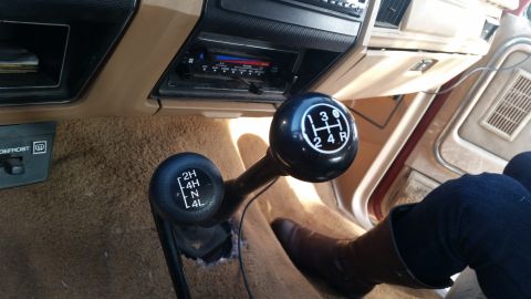 1985 Ford Bronco - The interior of a vintage Ford Bronco shows two gear shifters, one for the transmission and one for the 4x4 system. The shifters are black…