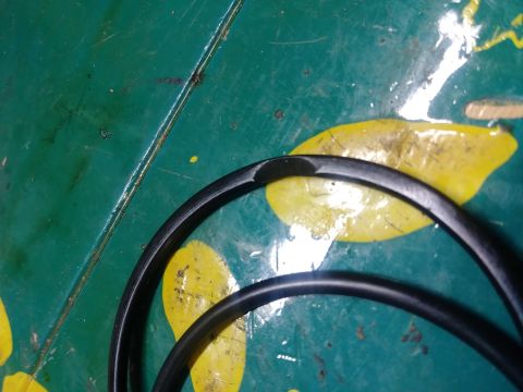 1996 Ford Bronco - A black rubber hose with a damaged section is coiled on a green surface with yellow markings.