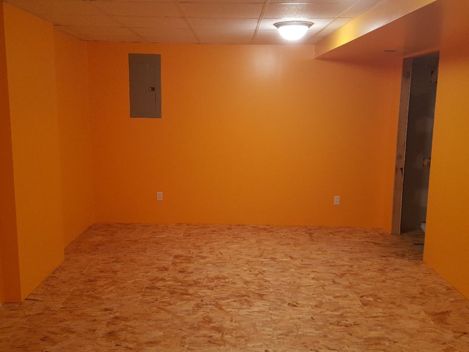 Unfinished basement room with orange walls and OSB subfloor.