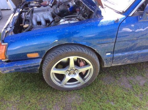 1992 Ford Bronco - A close-up, side view of the front fender and wheel of a blue vehicle. The engine bay is visible and open, with various components and hose…