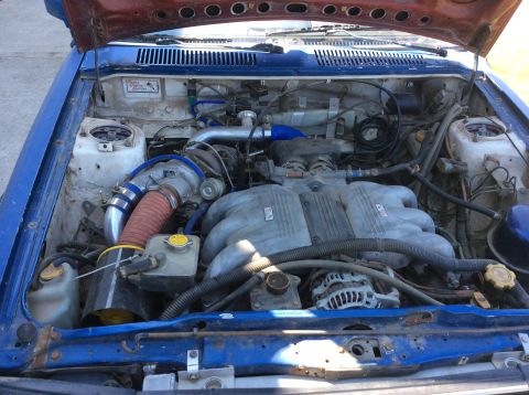 1992 Ford Bronco - The engine bay of a blue vehicle with a red hood is shown, featuring a turbocharger, intercooler piping, and a large intake manifold.