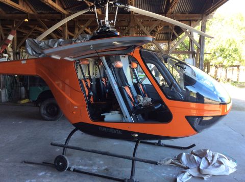 1992 Ford Bronco - An orange experimental helicopter is parked inside a wooden structure with its doors open, revealing the interior seating and harnesses. Th…