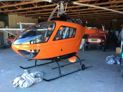 1992 Ford Bronco - An orange helicopter with "EXPERIMENTAL" written on its side is parked inside a wooden structure next to a red Toyota Land Cruiser.