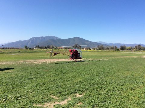1992 Ford Bronco - A red helicopter sits on a grassy field with mountains in the background under a clear blue sky.
