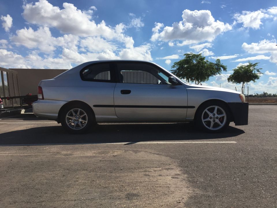 Silver two-door Hyundai Accent parked on asphalt with a trailer attached.