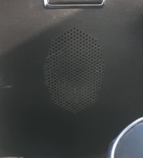 1995 Ford Bronco - A close-up view shows a speaker grille with many small circular perforations, set into a dark, textured surface. A metallic trim piece is v…