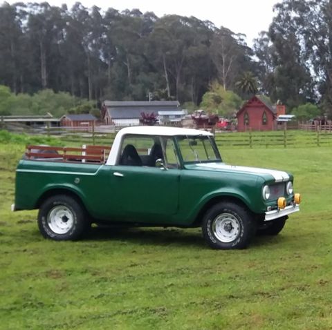 1991 Ford Bronco - A green and white International Scout pickup truck is parked on a grassy field with trees and buildings in the background.