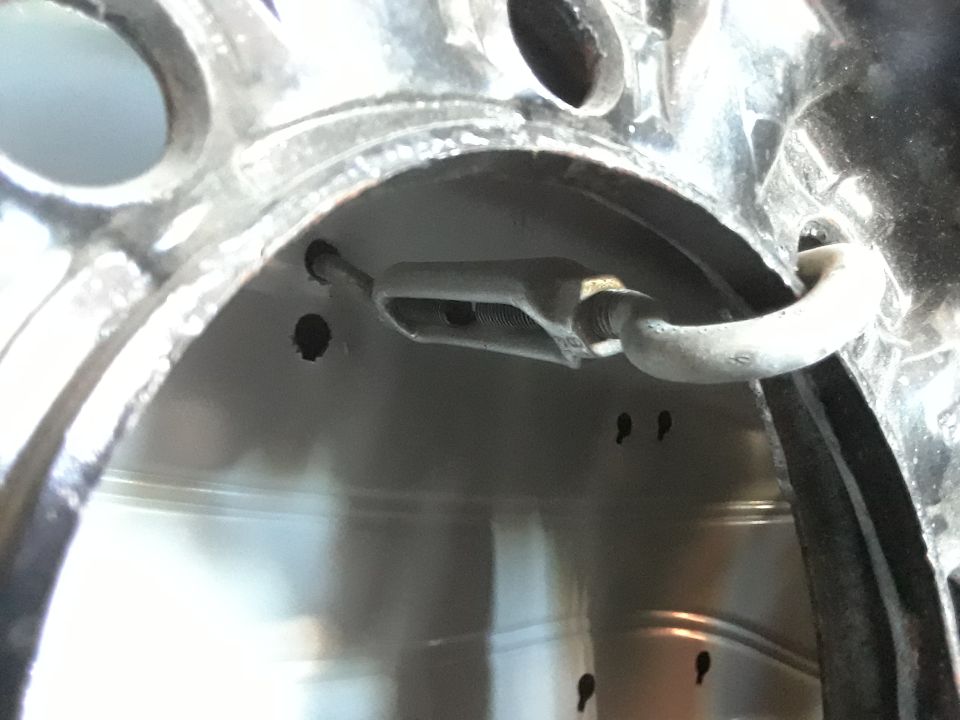 Close-up of a turnbuckle connected to a metal loop inside a vehicle's wheel well.