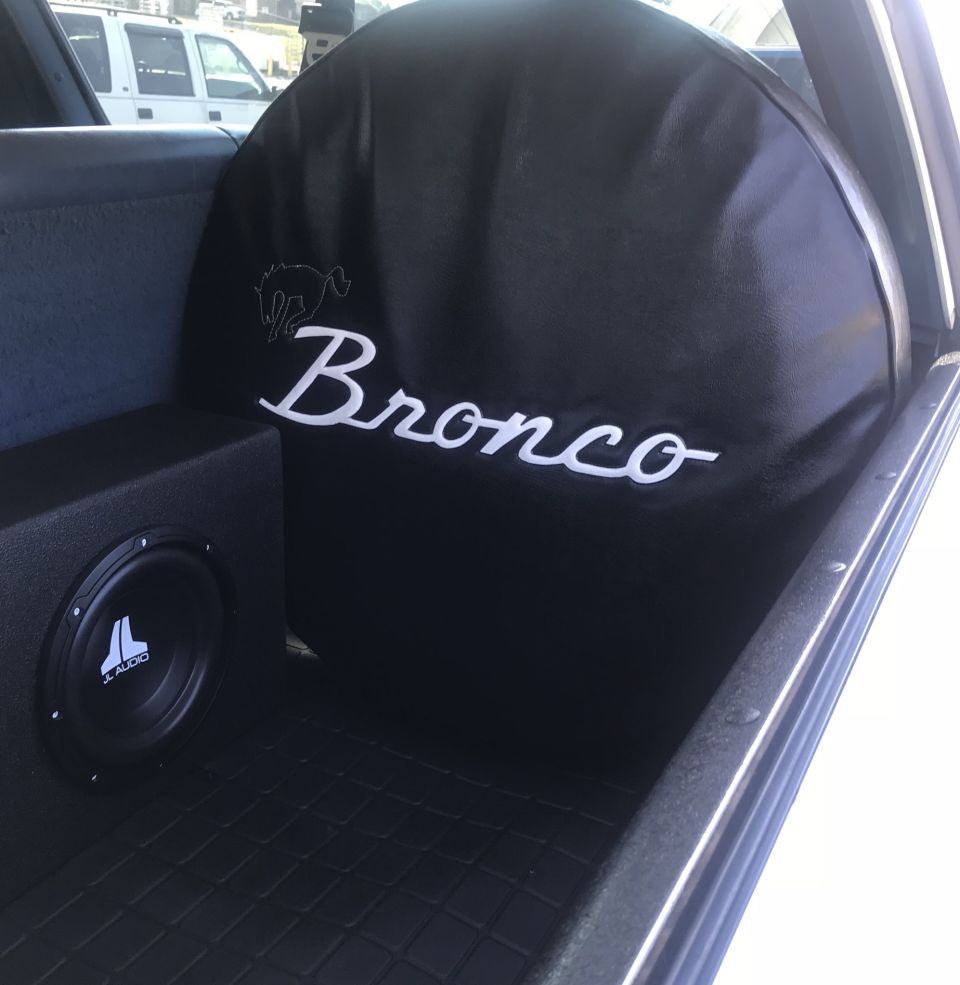 Black Bronco spare tire cover with white lettering and horse logo, JL Audio subwoofer box in cargo area
