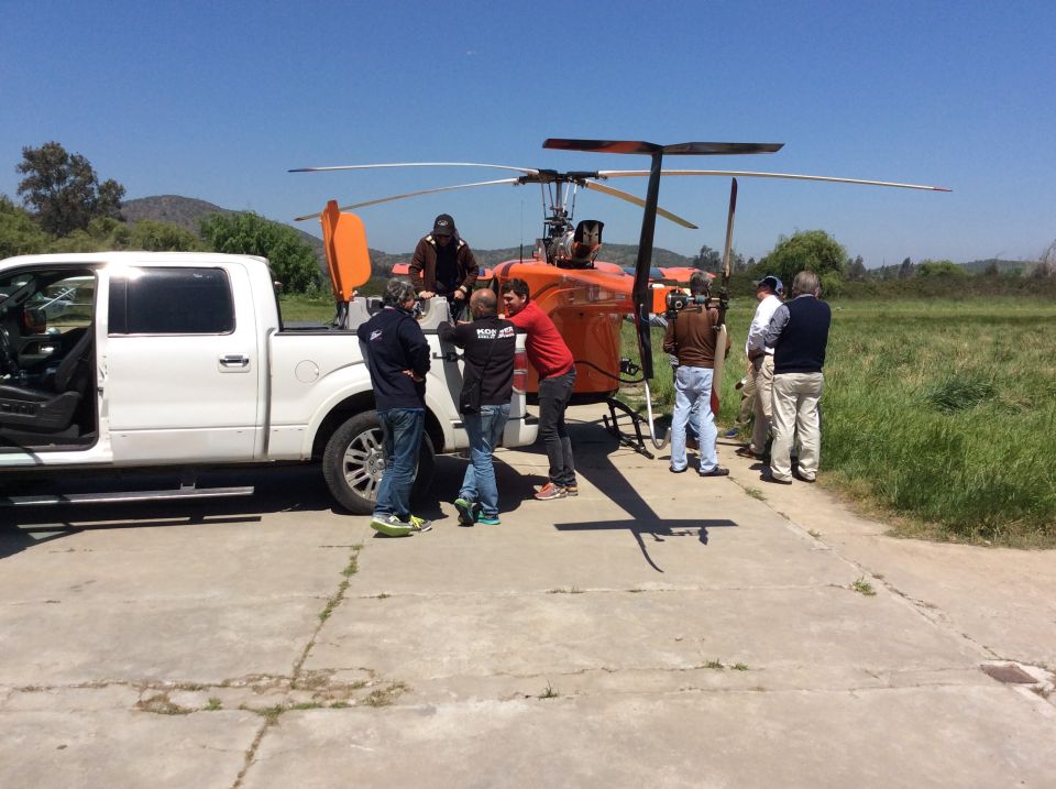 White pickup truck parked next to an orange helicopter with people around it
