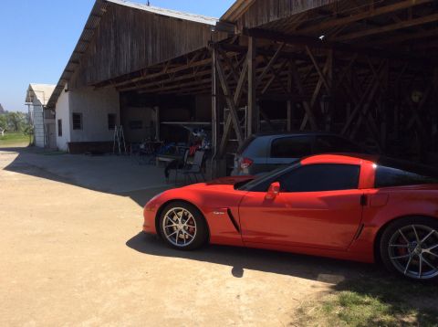 1992 Ford Bronco - A red sports car is parked outside a barn, with another vehicle visible in the background.
