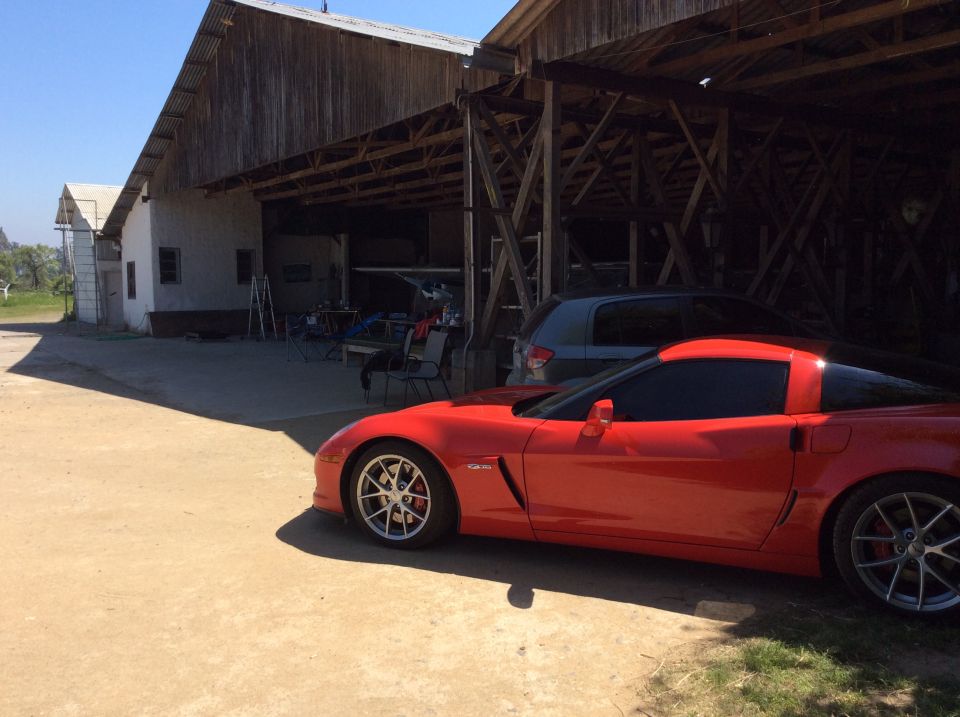 Red sports car parked in front of a barn, with a grey SUV behind it