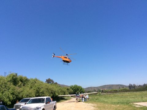 1992 Ford Bronco - An orange helicopter flies overhead near a small airplane and a white pickup truck on a sunny day.