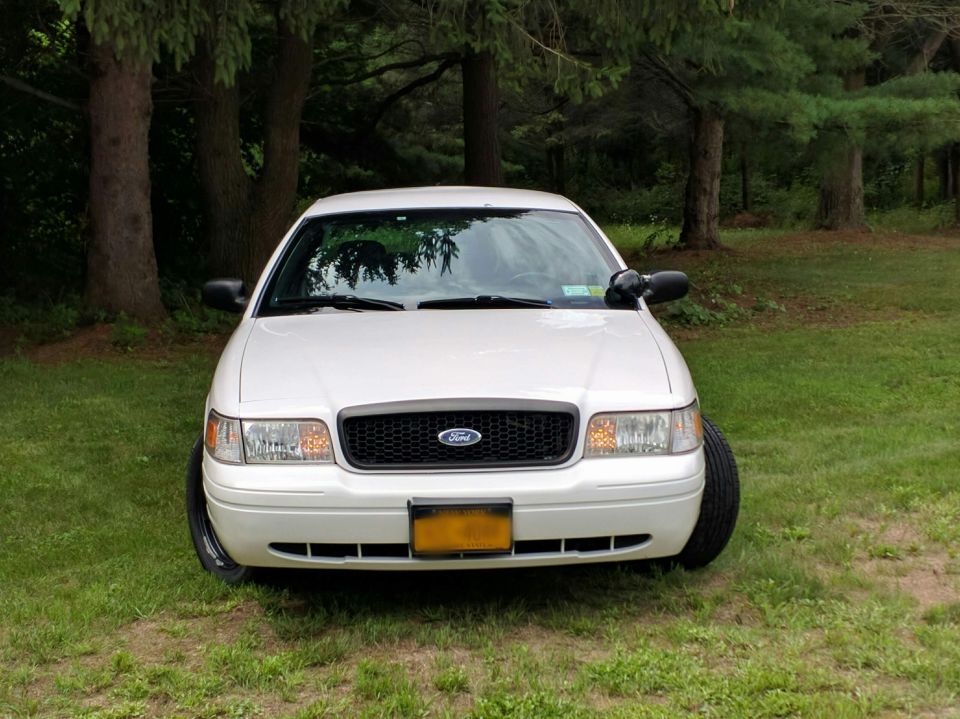 White Ford Crown Victoria parked on grass with trees in background
