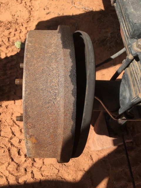 1995 Ford Bronco - Close-up of a rusty brake drum and rear suspension components on sandy ground.