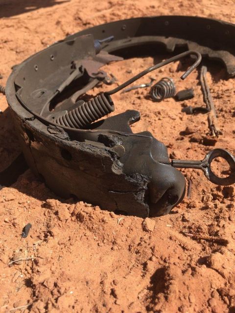 1995 Ford Bronco - This is a worn brake shoe assembly with its spring and hardware, lying on the dirt.