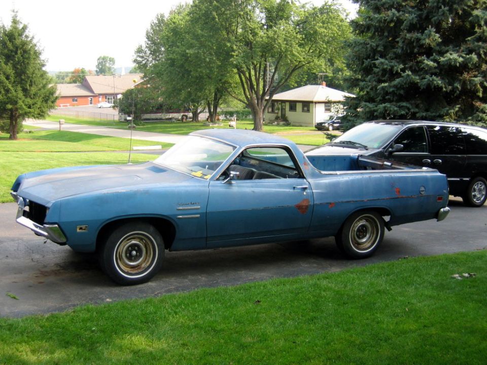 Blue 1970 Ford Ranchero with rust spots, parked on a driveway next to a black van