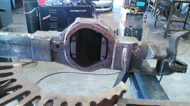 1978 Ford Bronco - A heavily modified rear axle housing is shown in a workshop setting, with welding equipment visible.