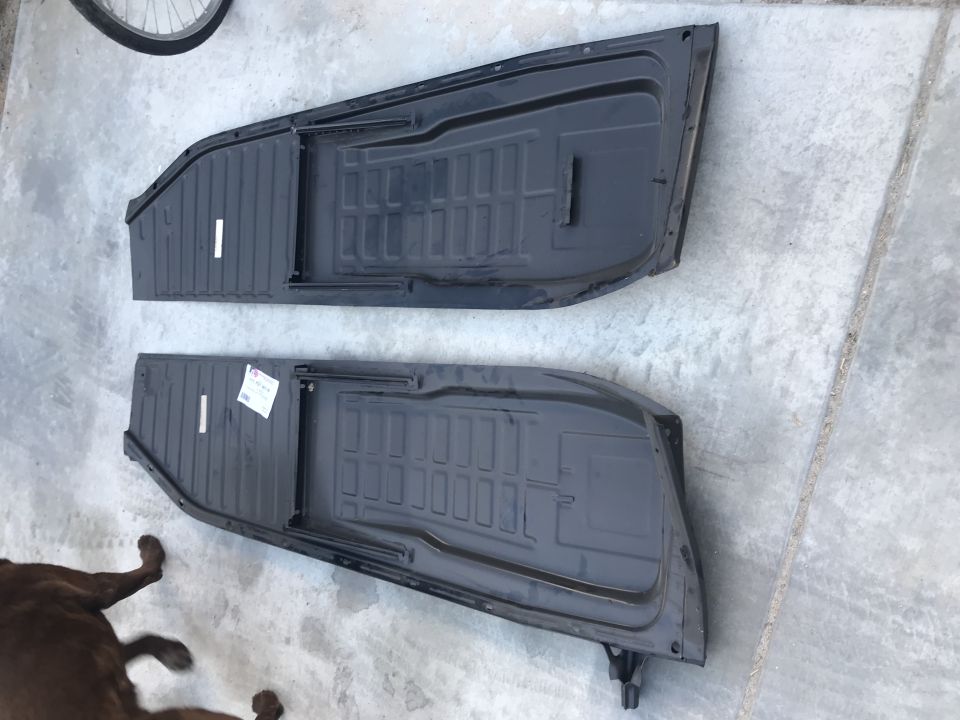 Two black metal floor pans for a classic Volkswagen Beetle on a concrete surface.