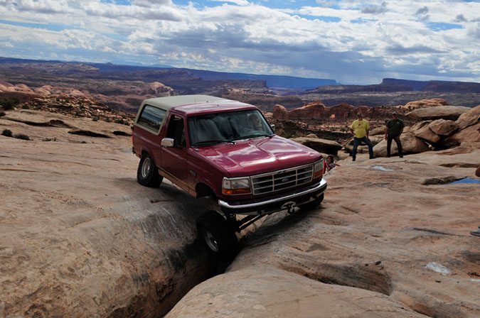 Red 1995 Ford Bronco driving over a rocky crevice on an off-road trail.