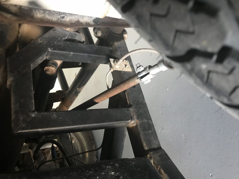 Undercarriage of a vehicle showing black frame, rusty rod, and tire.