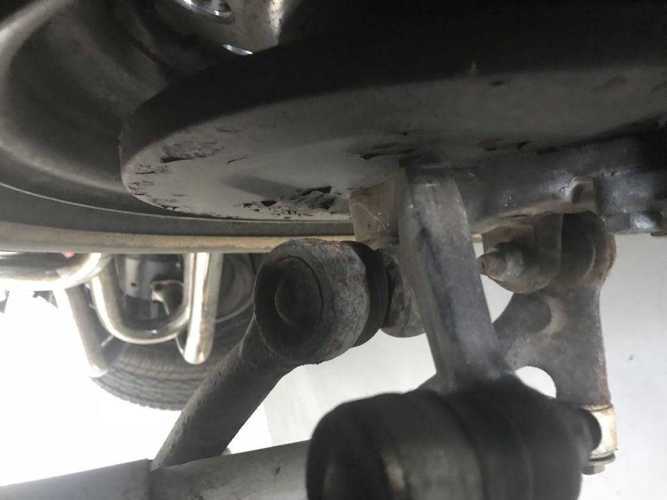 Underside view of vehicle suspension parts, control arms, bushings, tire, and exhaust.